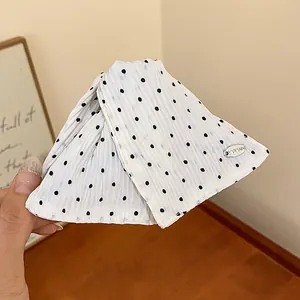 Detailweergave van een witte stoffen haarklem met zwarte stippen en een zilveren metalen accent