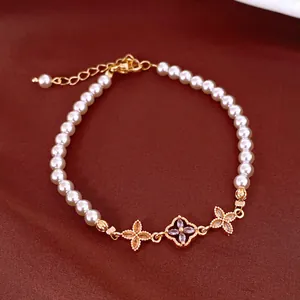 Close-up of elegant pearl bracelet with zircon flower charms and golden chain detail.