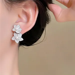 Detailansicht eleganter silberner Doppelblumen-Ohrringe mit Zirkonia und Perlen am Ohr.