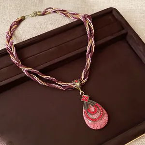 Détail d'un collier bohème avec pendentif goutte en strass rouges sur plateau brun