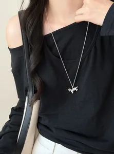 Close-up of a silver dog pendant necklace with bow detail worn on a black top.