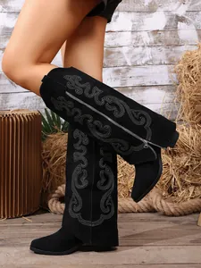 Detailed view of black embroidered western tall boots with pointed toe in a rustic setting