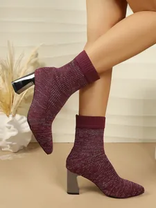 Close-up view of elegant burgundy glitter knit sock boots with block heels on model legs.