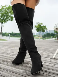 Detailed view of black faux suede pointed toe over-the-knee boots worn outdoors.
