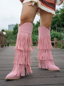 Stylish pink suede high-heeled boots featuring tiered long fringe on a wooden boardwalk.