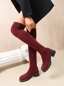 Close-up of burgundy over-the-knee sock boots with chunky mid heel and stretch knit fabric.