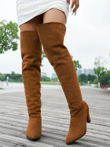 Detail view of brown suede pointed toe over-the-knee boots worn outdoors on a deck