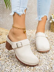 Dettaglio di sabot chiusi beige con fibbia decorativa e tacco alto in stile legno.