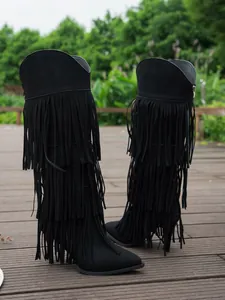 Detailed view of black suede fringe boots with high stiletto heels on a wooden deck