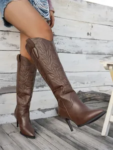 Elegant brown tall western boots with embroidery and stiletto heel on a rustic porch