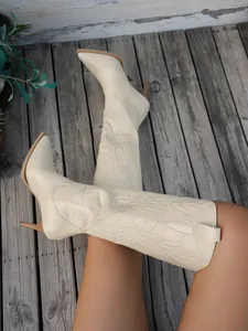 Detailed view of cream tall embroidered boots with pointed toe and stiletto heels on wood