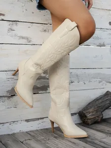 Detail of cream-colored embroidered knee-high boots with a pointed toe and slim high heel.