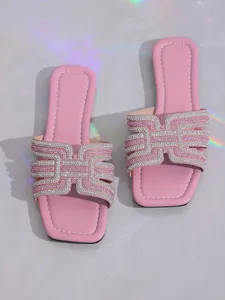 Close-up of pink flat slides featuring a decorative rhinestone H-strap design