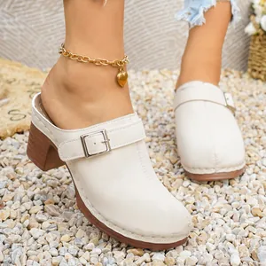 Eleganti sabot bianco crema con tacco largo e fibbia d'argento su fondo di ghiaia