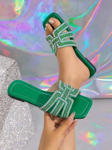 Close-up of green flat slide sandals with luxury rhinestone H-pattern strap detail.