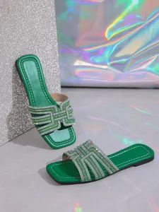 Close-up of green flat slide sandals with a shimmering rhinestone H-strap design.