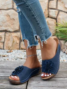 Vue détaillée de sandales compensées bleu marine avec fleurs ajourées sur un pont en bois