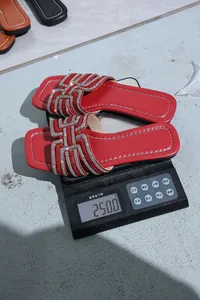 Red rhinestone flat slide sandals weighing 250 grams on a digital scale detail view.