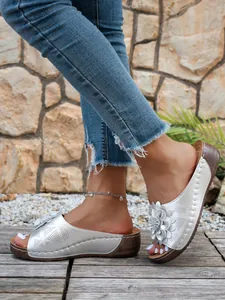 Élégantes mules compensées argentées avec fleurs et design ajouré portées dehors