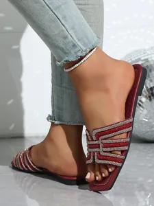 Detailed shot of stylish red flat sandals with shimmering rhinestone straps worn by model.
