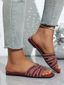 Close-up of stylish red flat sandals featuring intricate sparkling rhinestone-encrusted straps