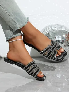 Close-up detail of black flat slides featuring sparkling rhinestone criss-cross straps