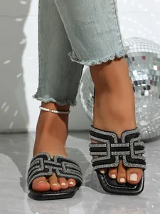 Close-up detail of black flat sandals with geometric rhinestone pattern on straps