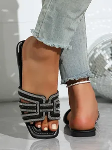 Close-up of black flat slide sandals with sparkling rhinestone embellishments and square toe