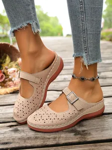Close-up of beige hollow-out platform clogs with floral patterns and buckle strap