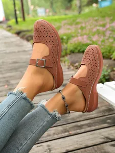 Close-up of brown hollow-out platform mules with decorative buckle strap and floral patterns.