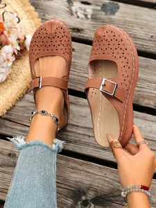 Detail of women's brown hollow-out wedge sandals featuring floral laser-cut patterns