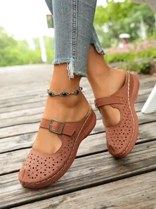 Close-up of brown hollow-out platform clogs featuring floral patterns and buckle