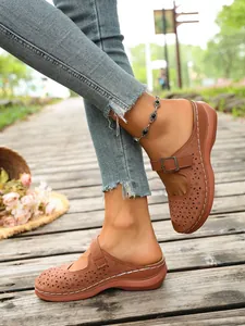 Detail shot of women's brown hollow wedge sandals with metal buckle on walkway.