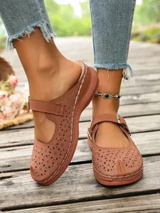 Close-up view of women's brown hollow-out platform sandals with buckle on wooden deck
