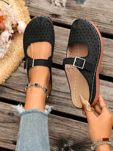 Close-up of black hollow-out floral wedge clogs with silver buckle strap on wooden background