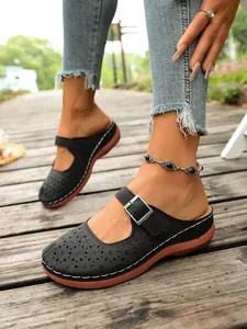 Detail view of black floral hollow-out mules with adjustable buckle on a wooden deck