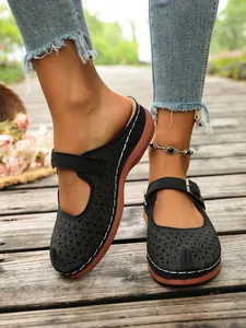 Black hollowed-out platform mules with adjustable buckle strap on wooden walkway