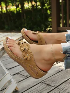Nahaufnahme von braunen Keil-Flip-Flops mit Blumenapplikationen und weißen Nähten.
