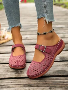 Detailed view of burgundy hollow platform clogs with buckle strap on a wooden boardwalk.