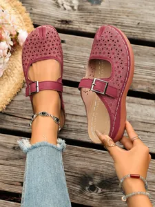Detailed view of burgundy wedge mule with intricate floral cutouts and buckle strap