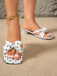 Elegant close-up of white polka dot sandals featuring a bow design and a low block heel