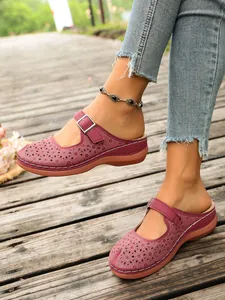 Women's burgundy hollow-out floral wedge clogs worn on a rustic wooden deck outdoor setting