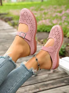 Close-up of pink hollow-out wedge mules with floral laser-cut patterns and buckle