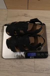Detaillierte Gewichtsmessung der schwarzen Riemchensandalen mit Leopardenmuster auf Waage