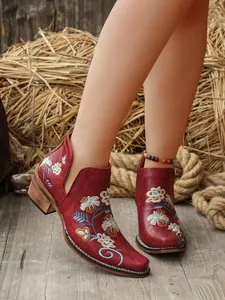 Primer plano de botas estilo western rojas con bordado floral en un entorno rústico