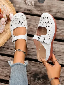 A detailed macro view showing the white hollow-out wedge mules with an adjustable buckle strap