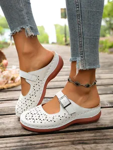Close-up detail of white hollow out platform mules with buckle strap on wooden floor