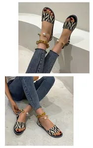 Detail view of zebra-print flat sandals with gold chain and pearl anklet decoration