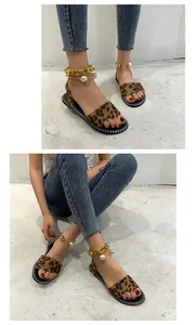 Close-up view of leopard print flat sandals featuring a chunky gold chain and pearl ankle strap