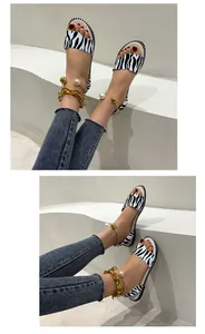 Detailed view of women's zebra print flat sandals with decorative gold ankle chain